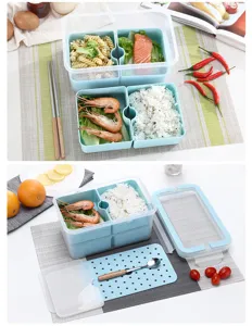 Detailansicht der mehrschichtigen Bento-Lunchbox mit Abtropfbrett und frischen Lebensmitteln.