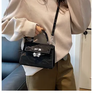 Vista de cerca de un bolso de mano negro texturizado para mujer estilo Kelly con herrajes.