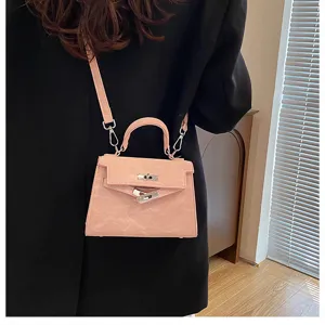 Detalle de bolso bandolera rosa con forma trapezoidal clásica, asa superior y cierre metálico.
