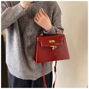 Vue détaillée d'un sac à main rouge en cuir verni avec fermoir doré et bandoulière.