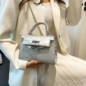 Bolso de mano metalizado texturizado plateado con correa y diseño trapezoidal clásico.