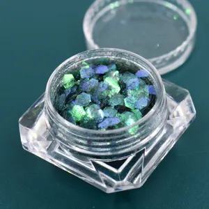 Dettaglio macro di fiocchi di glitter esagonali cangianti verdi e blu in un barattolo