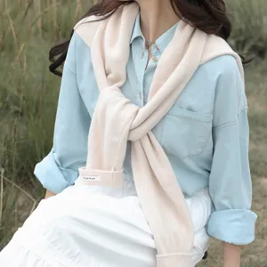 Detailansicht eines beigen Strickschals, gestylt über einem hellblauen Jeanshemd.