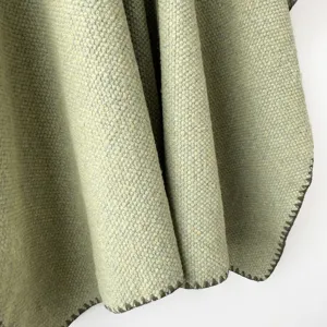 Detalle de tela de chal de punto verde claro, textura suave y borde de puntada oscura.