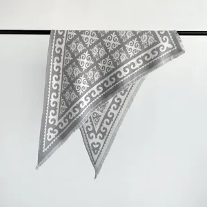 Close-up detail of grey jacquard scarf with delicate ethnic pattern and fringe edge texture.