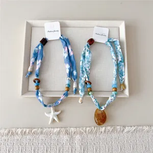 Gedetailleerd overzicht van blauwe bloemige stoffen ketting met houten kraal en hars hanger.