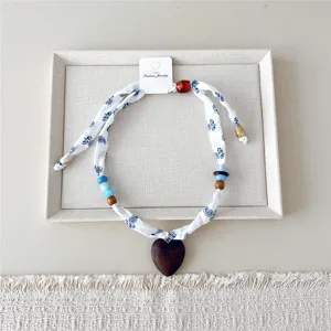 Close-up detail van chique stoffen lint ketting met houten hart hanger en kleurrijke kraaltjes.