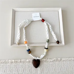 Gedetailleerd overzicht van een stoffen ketting met stippen, kleurrijke kralen en houten hart.