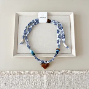 Detailopname van blauw-witte stoffen lintketting met kleurrijke kralen en hartvormige hanger.