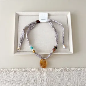Gedetailleerd uitzicht van deze smalle zijden sjaal ketting met kralen en hanger.