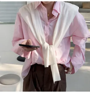 Detail shot of a solid color knit shoulder shawl worn over a pink shirt in a modern indoor setting.
