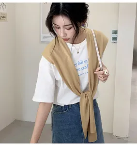 Detailed view of women's knitted shawl worn over a white t-shirt, casual summer fashion.