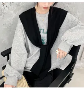 Detailed shot of stylish black knit shoulder shawl draped over grey sweatshirt in modern studio.