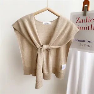 Knitwear detail shot showing the elegant shoulder cape design, fine texture and front tie accent.