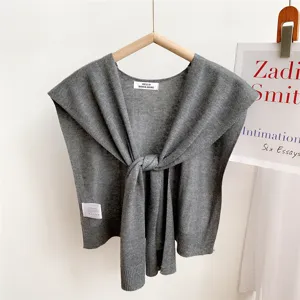 Close-up detail of grey knitted small cape shawl showing front knot design and brand label.