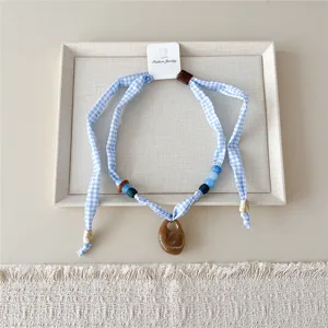 Blauwe gingham stoffen ketting sjaal met kraaltjes en bruine hanger voor chique accessoire.