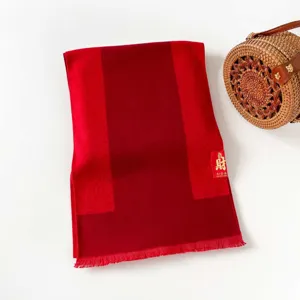 Detailed view of the vibrant red winter scarf with delicate fringes and auspicious tag.