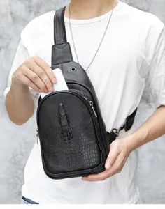 Detail view of black genuine leather chest bag with textured crocodile pattern worn by model.