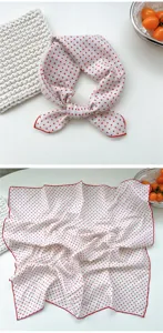 Detailed shot of a white cotton small square scarf featuring cute red polka dots and red rolled edges.