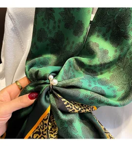 Primo piano dettagliato di sciarpa in seta verde con stampa floreale e anello di perle.