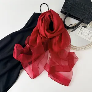Detail view of a luxurious sheer red silk scarf draped elegantly on black fabric setup.