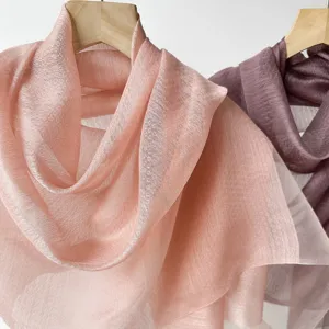 Close-up of lightweight sheer silk scarves in soft pink and mauve, hanging on wooden hangers.
