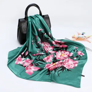 Detailed view of a green satin silk scarf featuring vibrant pink floral print draped on a chic black bag.