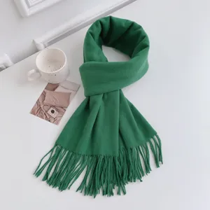 Close-up detail of a soft green winter cashmere-feel tassel scarf on clean white tabletop.