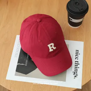 Close-up view of a red cotton baseball cap with embroidered letter detail on wooden table.