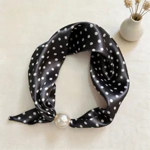 Close-up detail of a black polka dot silk scarf with an elegant pearl magnetic buckle.