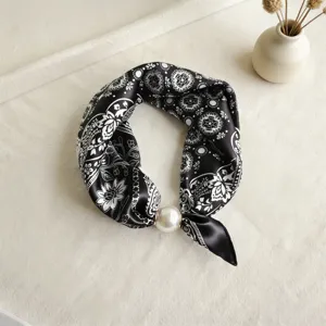 Vista detallada de un pañuelo de seda en blanco y negro con una elegante hebilla de perla.