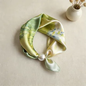 Detalle de pañuelo de seda verde degradado con un elegante cierre magnético de perlas.