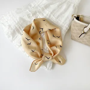 Detail van een beige zijden vierkante sjaal met minimalisten vogelprint, chic haar- en nekaccessoire.