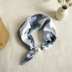 Detalle de cerca de pañuelo de seda con estampado de tinta azul y hebilla magnética de perla de lujo.