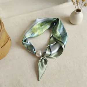Vista detallada del elegante pañuelo de seda verde con gran hebilla magnética de perlas.