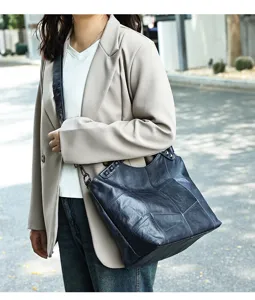 Close-up shot of the dark blue leather patchwork shoulder bag worn outdoors by a model.