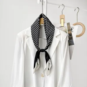 Close-up of elegant black and white striped silk scarf styled on white blazer hanger.