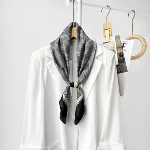 Detailed view of black and white houndstooth silk scarf with magnetic buckle on white blazer.