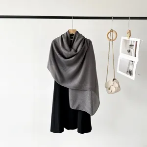 Detailed view of an elegant grey pleated scarf draped over a classic black dress on a hanger
