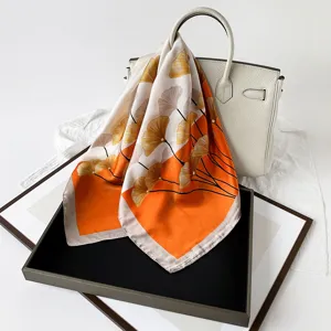 Detailansicht des eleganten Seidenschals mit Ginkgoblatt-Druck und leuchtend orangem Farbblock.
