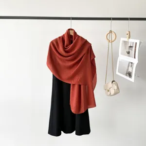 Detailed view of a terracotta pleated long scarf styled on a hanger with a black dress.