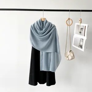 Detail view of light blue pleated scarf draped over black dress on a minimalist rack