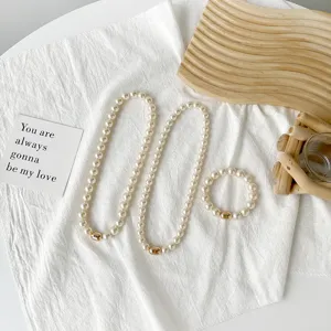 Detail shot of elegant pearl necklace and bracelet set with golden magnetic clasp on white cloth.
