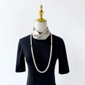 Detailed view of a chic floral small silk scarf and long pearl necklace on a mannequin display.