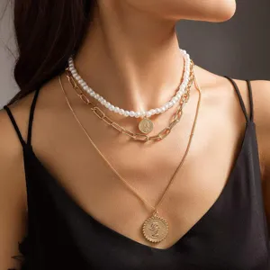 Close-up detail of multi-layered pearl and gold coin pendant necklace set worn on neck.