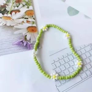 Primo piano di braccialetto con margherite di perline verdi su sfondo con tastiera in stile.
