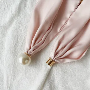 Close-up detail of luxury pink satin silk scarf with elegant pearl magnetic clasp and gold ring.