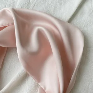 Close-up detail shot of an elegant light pink silk scarf, soft smooth fabric texture.