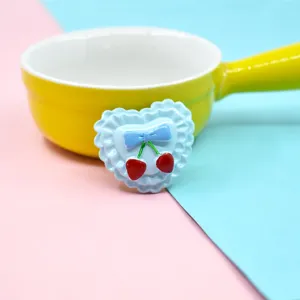 Detail showing a light blue heart-shaped resin accessory with a bow and cherries