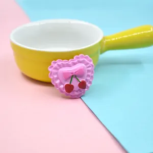 Macro detail of a pink resin heart accessory with cherry and bow motif for DIY crafts